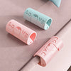 Three non-slip bed sheet grippers in pink and light blue colors are shown on a beige fabric surface.
