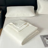 White ice silk cooling comforter folded on a white bed with a white quilted pillow.