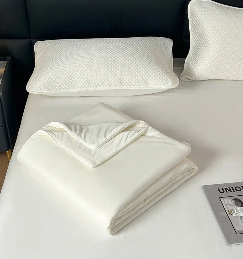 White ice silk cooling comforter folded on a white bed with a white quilted pillow.