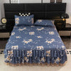 A navy blue floral bed skirt with a ruffled hem is displayed on a bed, against a dark headboard.