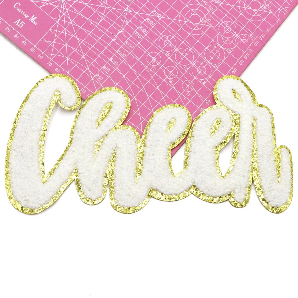 Gold glitter embroidered cheer letter patch on a pink cutting mat