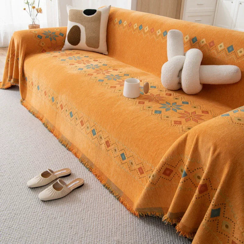 An orange bohemian accent sofa cover draped over a sofa with patterned fabric and a small white mug.