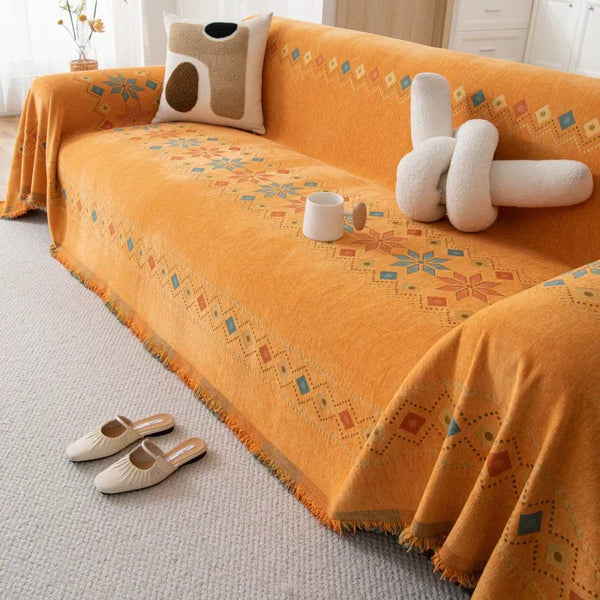 An orange bohemian accent sofa cover draped over a sofa with patterned fabric and a small white mug.
