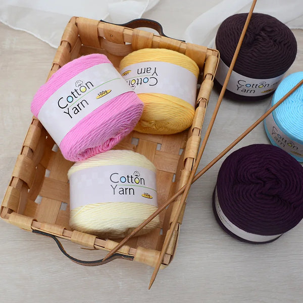 A wooden basket filled with various skeins of hand-knitting cotton yarn in pink, yellow, purple, and blue.