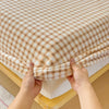Hands are pulling up a beige and brown plaid flannel fitted sheet with deep pockets.