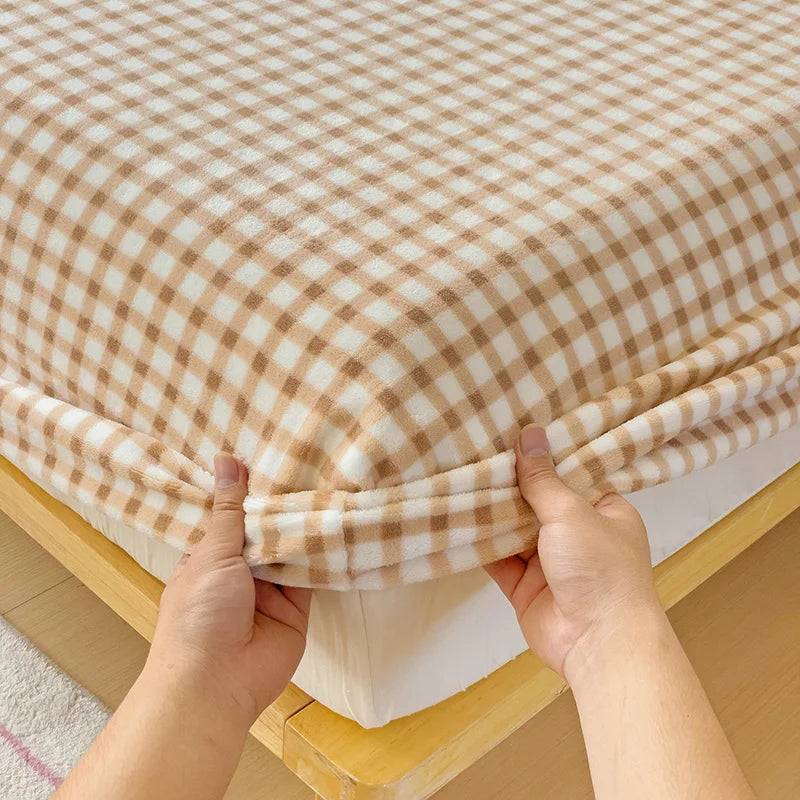 Hands are pulling up a beige and brown plaid flannel fitted sheet with deep pockets.