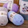 A collection of purple, gray, and light blue chenille yarn balls displayed on a wooden surface.