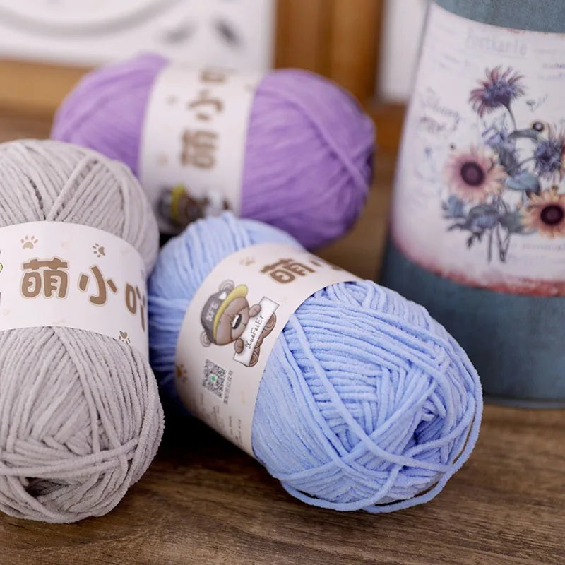 A collection of purple, gray, and light blue chenille yarn balls displayed on a wooden surface.