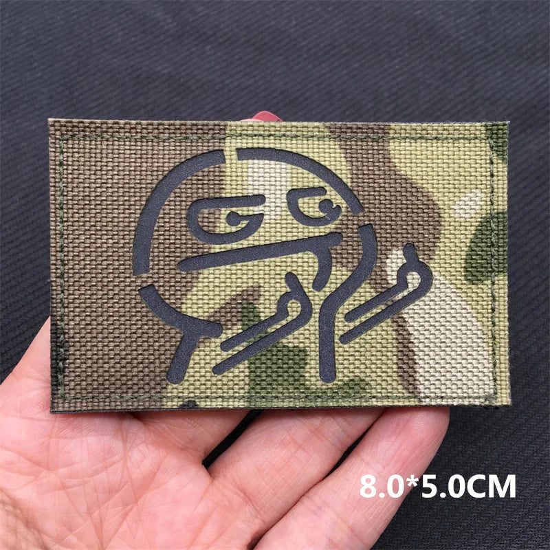 A close-up of a tactical multicam national flag patch with a stylized face design shown on a hand.