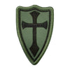A dark olive green shield-shaped patch embroidered with a black cross design.
