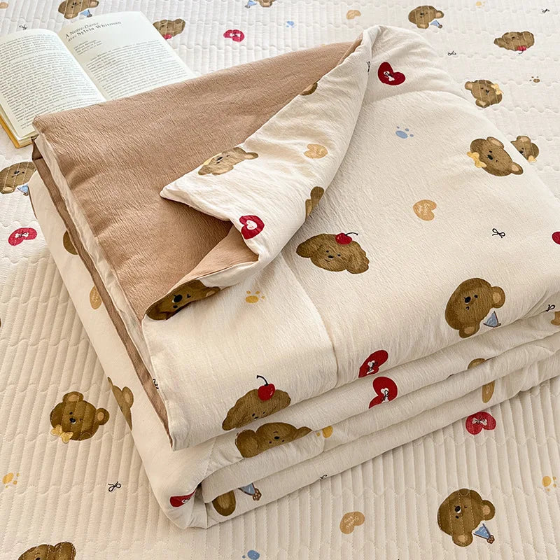 A beige cartoon quilting comforter with scattered bear and heart patterns is displayed on a white quilted surface.