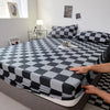A black and white checkered fitted sheet is laid out on a bed, with pillows and decorative items visible.