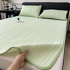 A hand is touching a light green cooling ice silk bed pad on a bed, showing its ribbed texture.