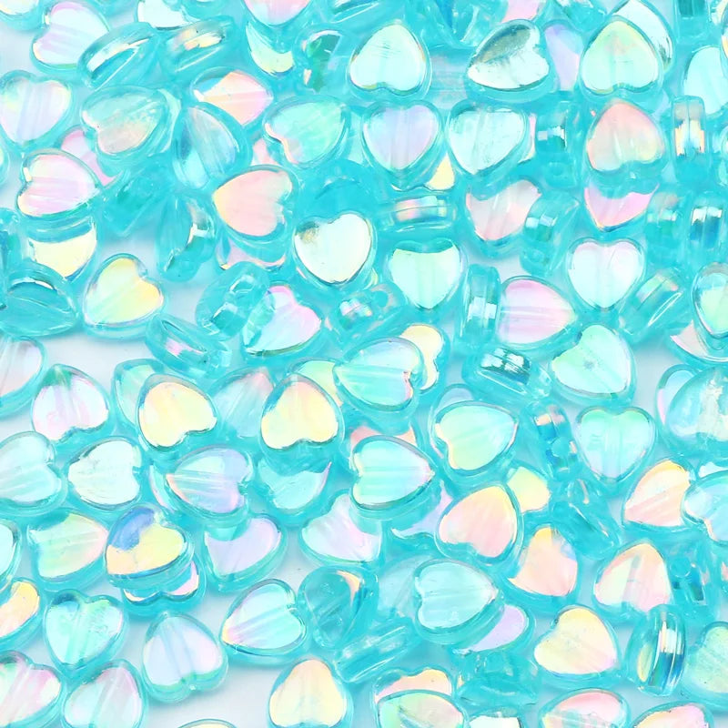 A close-up of a 100-pack of clear, iridescent blue acrylic heart beads for jewelry making.