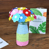 A bouquet of colorful felt flowers in various shades of pink, blue, yellow, and red displayed in a glass vase.