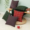 A set of two plaid decorative throw pillow covers in green and red tartan fabric displayed on a wooden surface.
