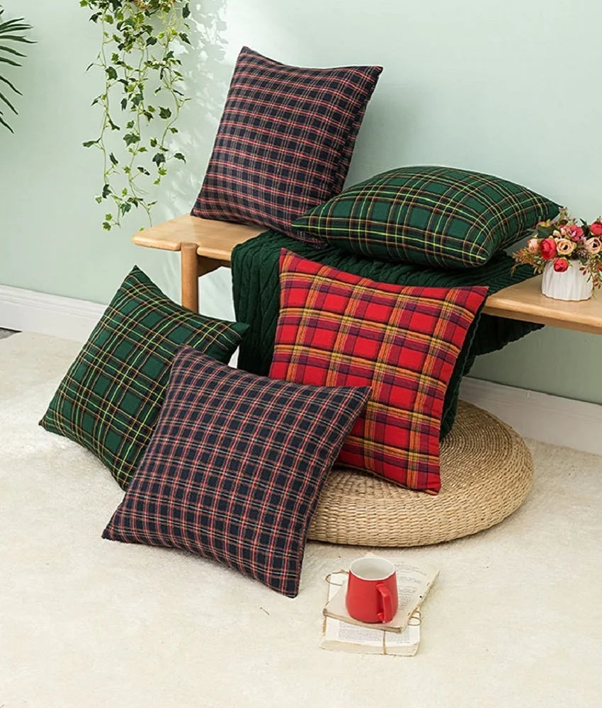 A set of two plaid decorative throw pillow covers in green and red tartan fabric displayed on a wooden surface.