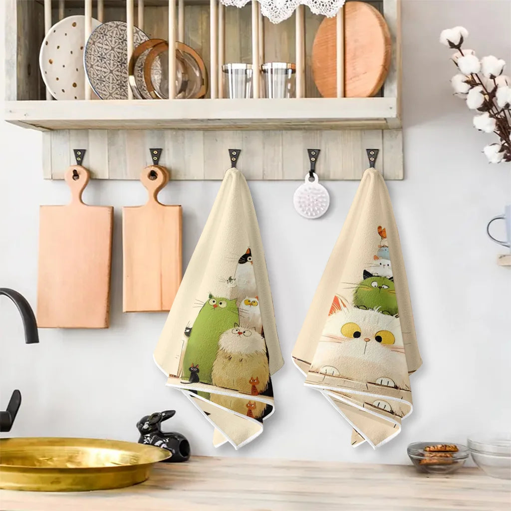 A set of two light beige kitchen towels featuring cute cat designs hanging on a wall.