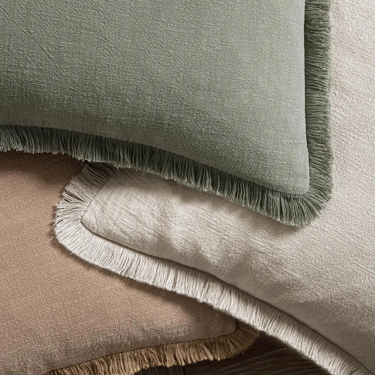 A close-up of a linen fringe throw pillow cover in sage green and beige tones.