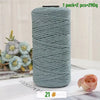 A roll of medium-thick, teal-colored hand-woven cotton yarn for crafting, shown next to a pink rose.
