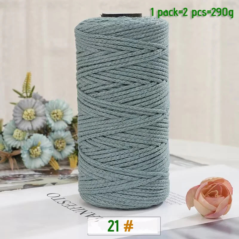 A roll of medium-thick, teal-colored hand-woven cotton yarn for crafting, shown next to a pink rose.