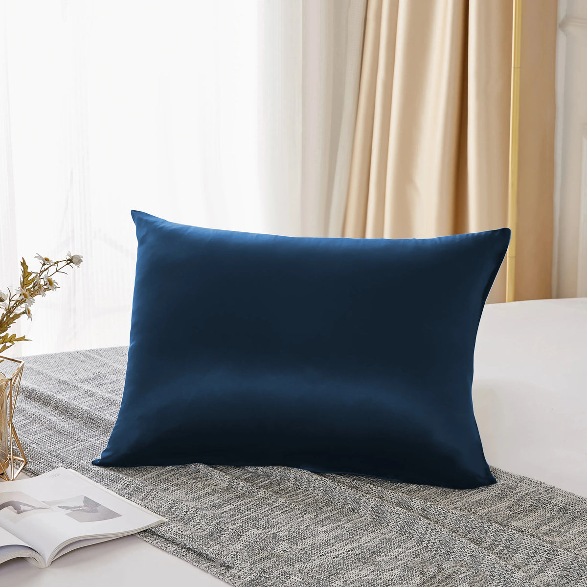 A dark blue pure mulberry silk pillowcase resting on a gray fabric next to a window.