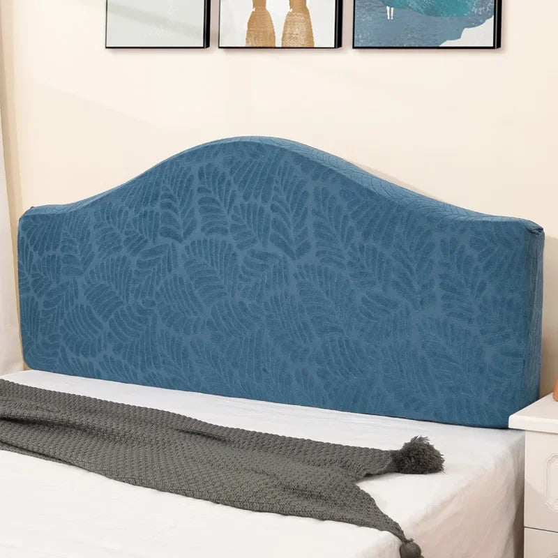 A navy blue soft elastic headboard cover with a leaf pattern displayed on a white bed.