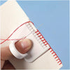 A hand is using a precision sewing guide template kit with a red thread to mark a seam on white fabric.