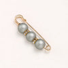 A delicate gold-toned adjustable pearl brooch featuring three spherical gray beads accented with small clear stones.