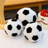 Three realistic football plush toys in black and white are displayed on a white surface next to a cake.