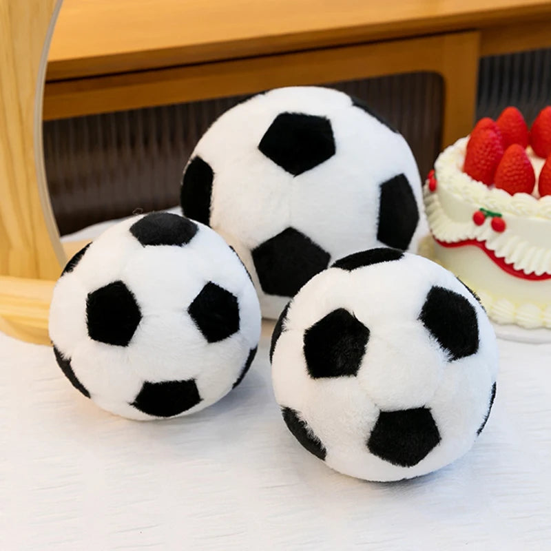 Three realistic football plush toys in black and white are displayed on a white surface next to a cake.