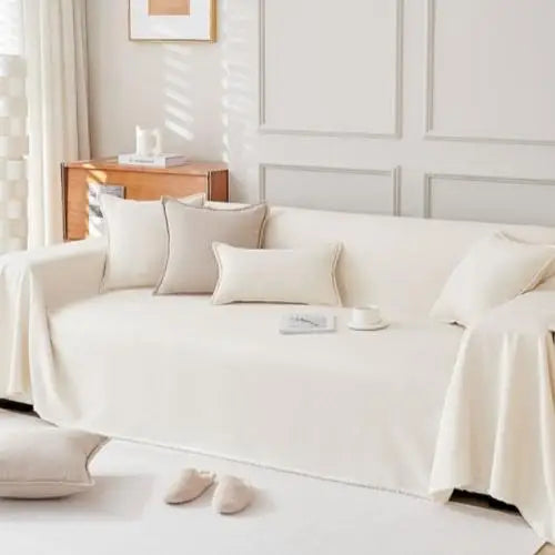 A white anti-scratch sofa cover draped over a light-colored sofa with decorative pillows.