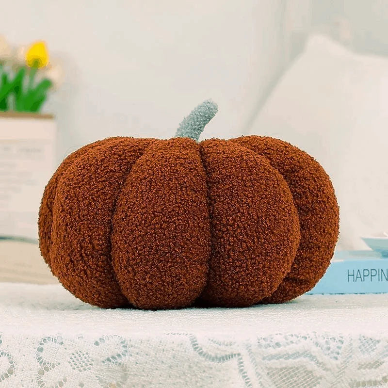 A round, textured brown pumpkin shaped throw pillow with a light blue stem resting on a white lace surface.