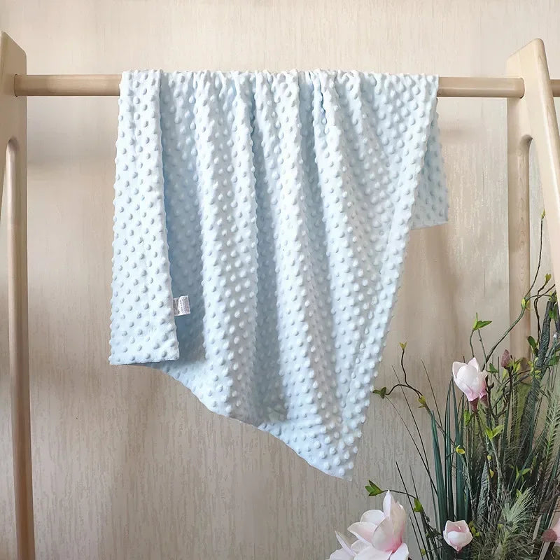 Light blue fleece swaddle blanket with a textured pattern hanging on a wooden rack.