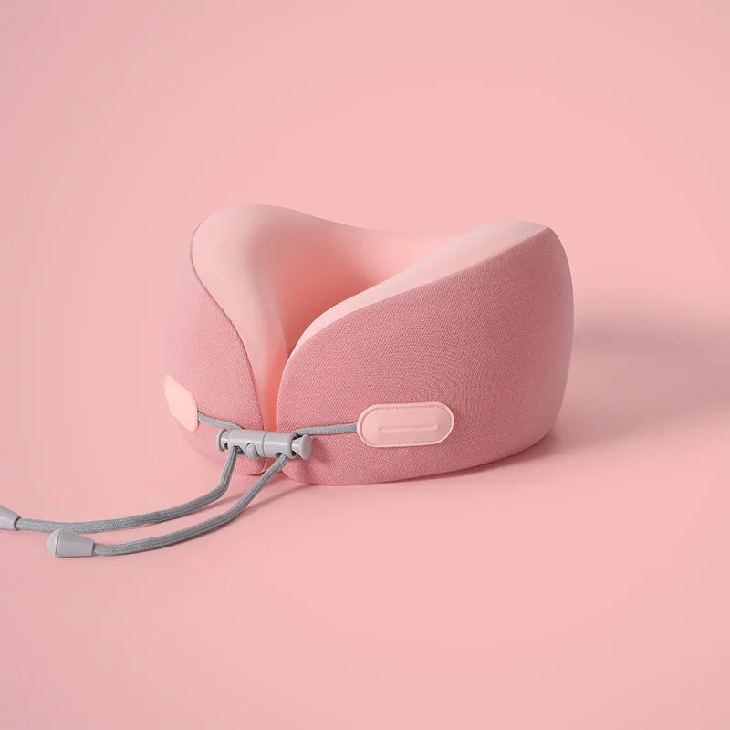 A pink U-shaped memory foam travel neck pillow with a cooling cover resting on a light pink surface.