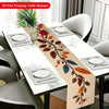 A beige floral branch table runner with leaves and berries is displayed on a white dining table set for a meal.