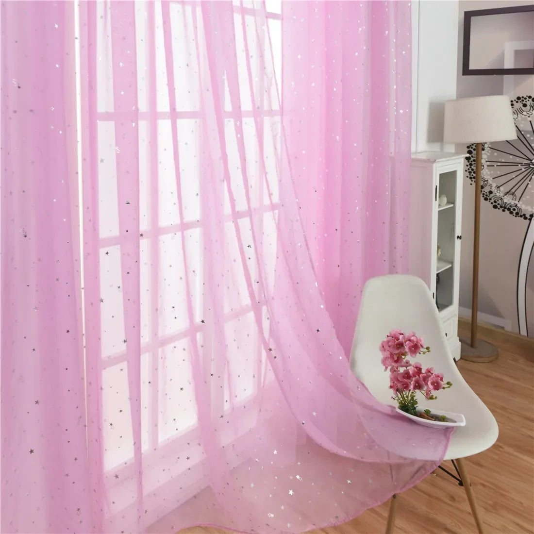 Pink tulle curtains with silver stars covering a window in a bright room.