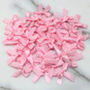A pile of pink satin ribbon bows for crafts and decor scattered on a white marble surface.