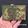 A rectangular tactical patch featuring a dark silhouette of a medical cross on a camouflage background being held by a hand.
