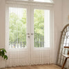 White decorative fabric door curtain with tassel trim covering a glass door.