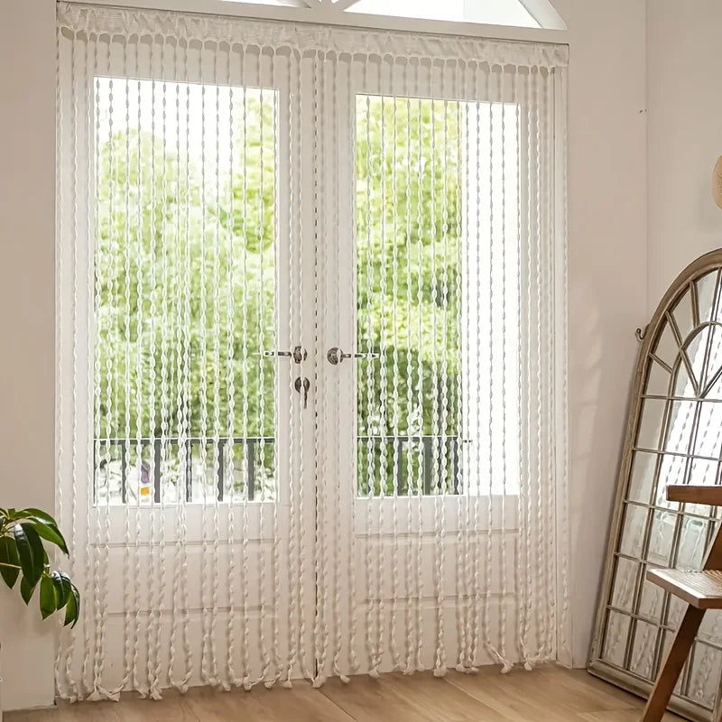 White decorative fabric door curtain with tassel trim covering a glass door.