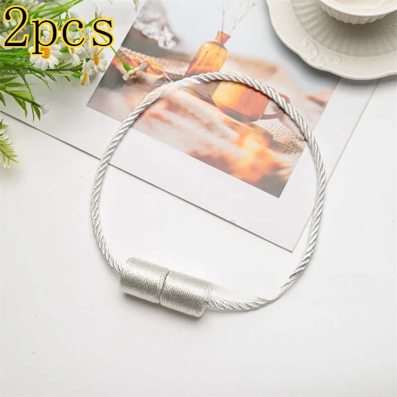 Two silver magnetic curtain tieback rings on a white background with a blurred photo in the background.
