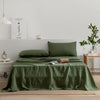 A green pure French linen bed sheet is spread on a bed with a matching pillow and a framed Chanel print in the background.