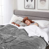 A couple sleeping under a gray sherpa fleece blanket in a bright bedroom.