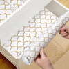 A roll of white silicone non-slip drawer liner with a gold geometric pattern is being pulled out of a storage box.