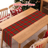 A wooden table is decorated with a red and green tartan Christmas table runner and plaid cushions.