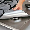 A hand is placing a silver reusable gas hob protector liner onto a stovetop burner.