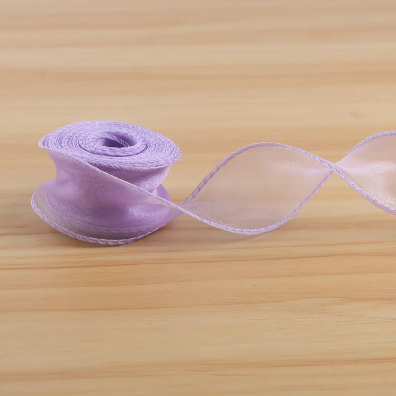 A roll of light purple satin ribbon unwinding into a sheer, flowing ribbon on a wooden surface.