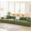 A modern, olive green stretchable sofa slipcover with white cushions and a black and white patterned rug in a bright room.