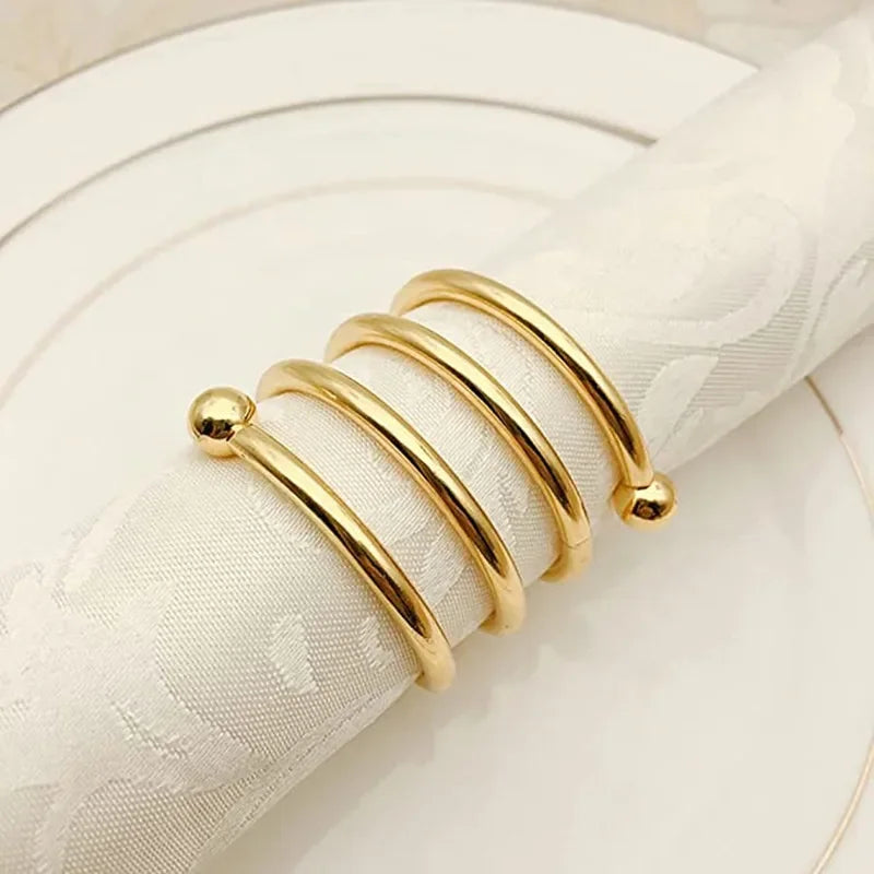Gold metal napkin rings displayed on a white plate with a cream-colored linen napkin.